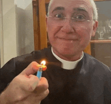 a priest is holding a lit lighter in his hand and smiling .