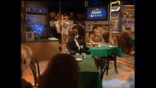 a woman is sitting at a table with a green tablecloth in front of a television that says kino bazar .