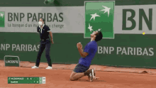 a man in a blue shirt is kneeling down on a tennis court in front of a bnp pariba sign .