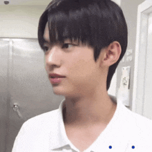 a young man with black hair and a white shirt is standing in front of a stainless steel door .