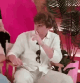 a man in a white shirt is sitting in a chair with his hand to his mouth .