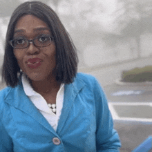 a woman wearing glasses and a blue jacket looks at the camera