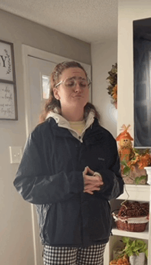 a woman wearing a black jacket and glasses is standing in a room