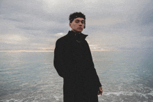 a man in a black coat stands on the beach