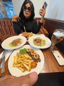 a woman sitting at a table with plates of food and a phone