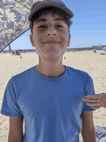 a young boy wearing a hat and a blue shirt is standing on the beach