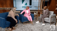 a woman in a pink suit is sitting in a chair talking to two men