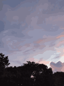 a sunset sky with trees in the foreground and a few clouds in the background