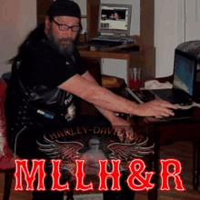 a man sitting at a desk with a laptop and a harley-davidson logo on his shirt