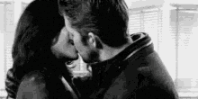 a black and white photo of a man and woman kissing in front of a window .