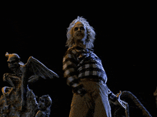 a man in a plaid shirt is standing in front of a statue of a demon