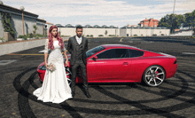 a bride and groom pose in front of a red sports car in a parking lot