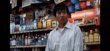 a man in a striped shirt is standing in front of a store shelf with bottles of liquor on it ..