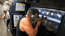 a man is aiming a rifle in a shooting range with a warning sign on the wall