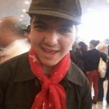 a young man wearing a hat and a red scarf is standing in a crowd .