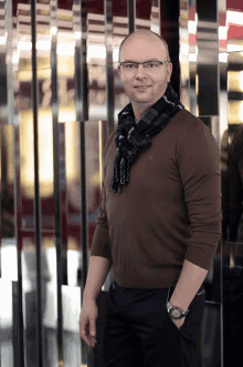 a man wearing glasses and a scarf stands in front of a mirrored wall