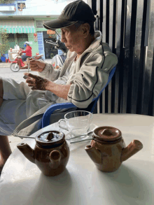 a man sits at a table with two teapots and a cup