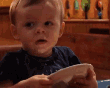 a young boy is sitting at a table with a plate in his hand and making a funny face .