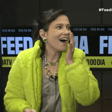 a woman wearing a neon yellow jacket stands in front of a sign that says feed do dia