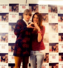 two women are making a heart shape with their hands in front of a wall with red posters