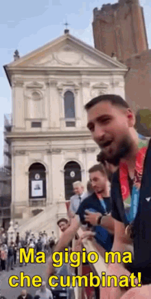 a man with a medal around his neck is standing in front of a building and talking to a crowd .