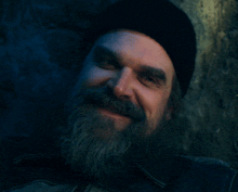 a man with a beard wearing a black hat looks at the camera