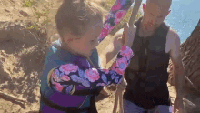 a man and a little girl are holding a rope . the little girl is wearing a life jacket .