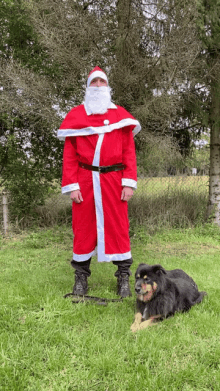 a man in a santa claus costume stands next to a black dog