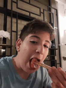 a young man in a blue shirt is eating a piece of food with chopsticks