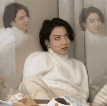 a man in a white turtleneck sweater is sitting in front of a mirror making a funny face .