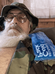 a man with glasses and a beard is laying on a couch with a bag of back cold