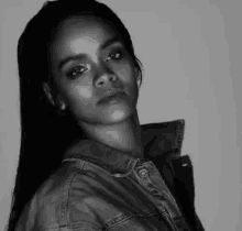 a black and white photo of a woman wearing a denim jacket and looking at the camera .