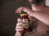 a man without a shirt is opening a jar of sauce