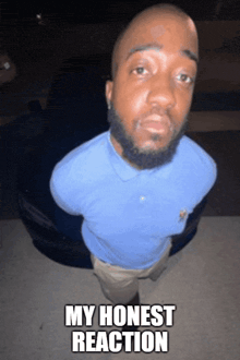 a man in a blue shirt is standing in front of a black car with the words my honest reaction above him
