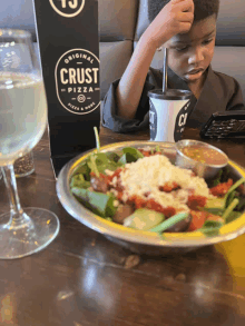 a child sits at a table with a plate of food and a cup of soda from crust pizza