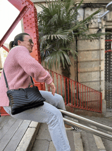 a woman wearing a pink sweater is sitting on a railing