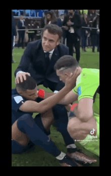 a man in a suit and tie is kneeling down next to a soccer player on the field