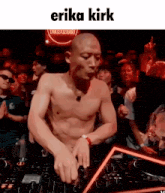 a man without a shirt is playing music in front of a crowd with the name erika kirk written above him