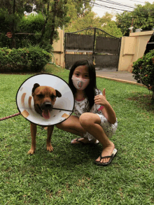 a girl wearing a mask kneeling next to a dog with a cone on its head