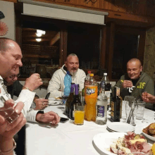 a group of men sit at a table with bottles of fanta