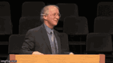 a man in a suit and tie is standing behind a wooden podium in front of an empty auditorium .