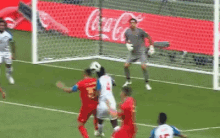 a group of soccer players are playing a game of soccer on a field with a coca cola ad in the background .