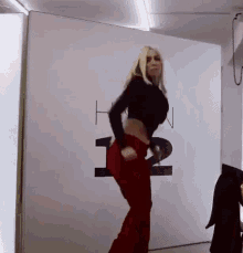 a woman in a black crop top and red pants is dancing in front of a wall that has the number 12 on it