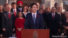 a man in a suit and tie stands at a podium in front of a large group of people .