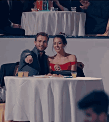 a man and a woman sit at a table pointing