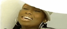 a woman wearing a white hat and hoop earrings is smiling .