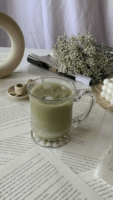 a cup of iced green tea sits on a table next to a book and flowers