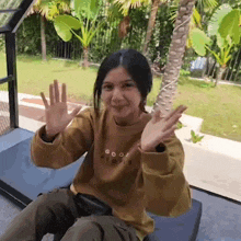 a woman wearing a sweatshirt that says good people is waving at the camera while sitting on a couch .