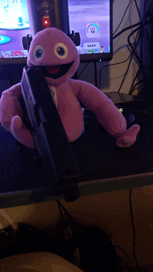 a purple stuffed animal is holding a gun in front of a computer monitor that says back on it