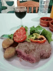 a plate of food with tomatoes lettuce and potatoes next to a glass of wine